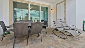 An outdoor patio with a table and chairs, a glass door leading to a covered area, and a door to the right. - Super Snug- FUN Themes Pool Tons OF Amenities (Kissimmee)