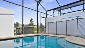 An indoor swimming pool with clear blue water, surrounded by a metal frame structure, and a view of the outside through large windows. - Super Snug- FUN Themes Pool Tons OF Amenities (Kissimmee)
