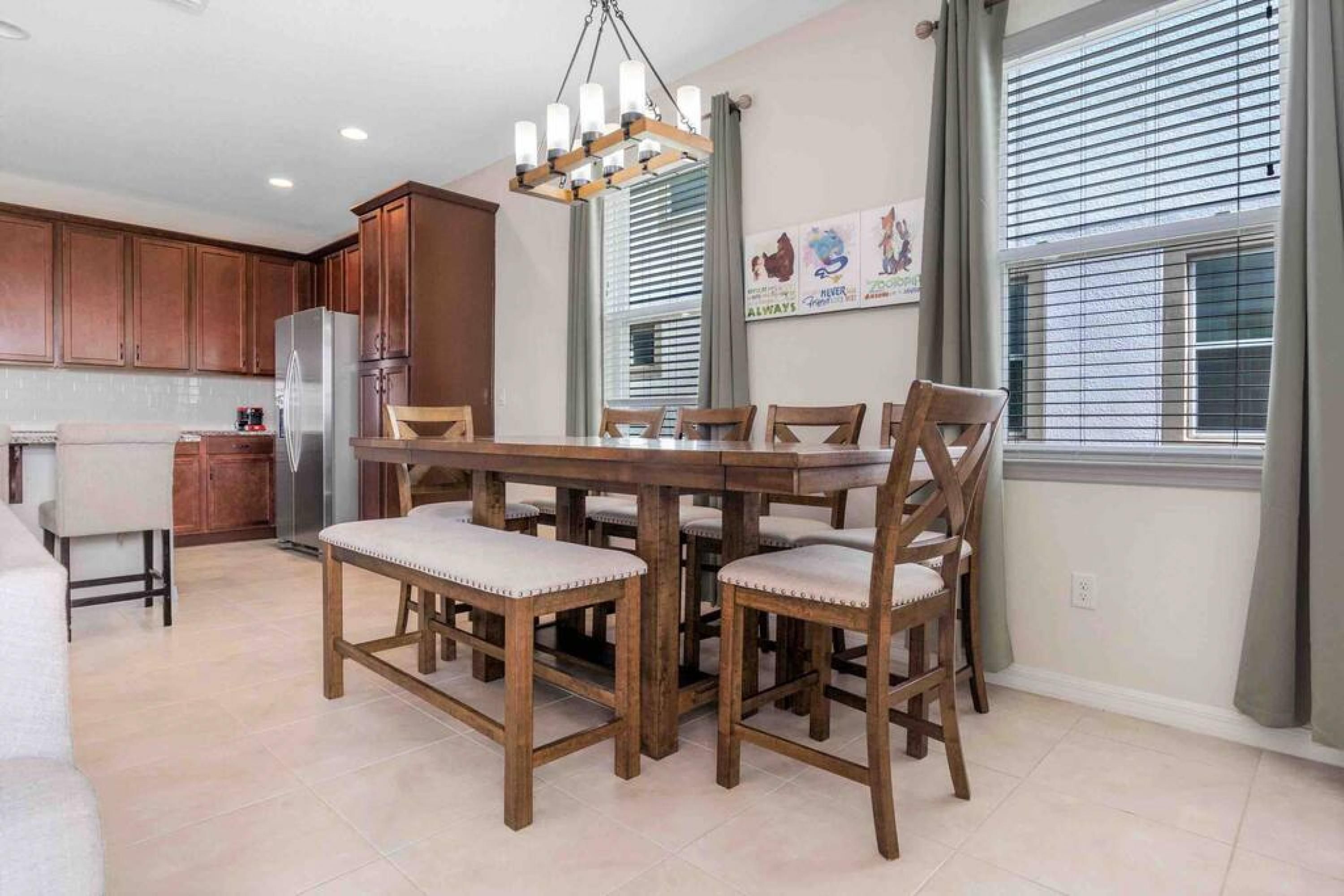 Comedor con mesa y sillas de madera, una araña y una cocina al fondo.