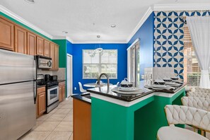 A modern kitchen with a teal island, stainless steel appliances, and a blue accent wall. - Super Fly- Movie Loft w Recliners Near Disney (Kissimmee)