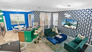 Una sala de estar moderna con un sofá verde, un reposapiés azul y un comedor con una isla verde y sillas blancas.