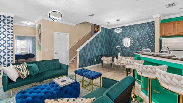 Una sala de estar moderna con un sofá verde, un otoman azul y una zona de cocina con una barra verde y taburetes blancos.
