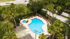 Vista aérea de un resort con una gran piscina, palmeras y un edificio pequeño con techo de paja.