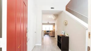A hallway with a red door, a staircase, and a living area in the background. - Super Liked - 4BD 3 5b 6 Miles To Disney Springs (Kissimmee)