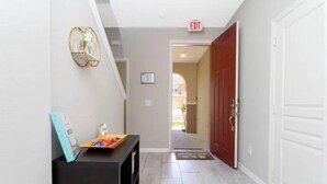 A hallway with a black console table, a wall-mounted decorative item, and a red door at the end. - Super Liked - 4BD 3 5b 6 Miles To Disney Springs (Kissimmee)