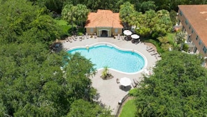 An aerial view of a resort with a swimming pool surrounded by lounge chairs and umbrellas, a building with a tiled roof, and lush greenery. - Super Liked - 4BD 3 5b 6 Miles To Disney Springs (Kissimmee)