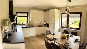 A modern kitchen with white cabinets, a black countertop, and a dining area with a table set for two. - Vila Minka - Your Perfect Bled Getaway (Bled)