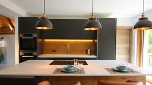 Een moderne keuken met donkere kastjes, een centraal eiland met een wit aanrechtblad en hangende lampen.