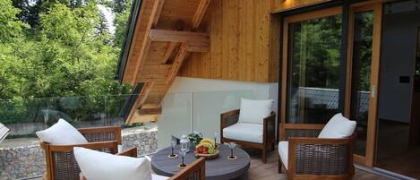 A wooden deck with wicker furniture and a round table, surrounded by glass doors leading to a covered area.