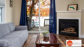 A living room with a sofa, a wooden coffee table, a fireplace, and a view of a dock and trees. - Rest and Relaxation Z s at Slayton Lake (Belding)