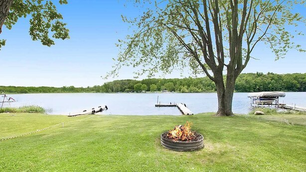 A lakeside property with a grassy area, a fire pit, a dock, and a tree. - Rest and Relaxation Z s at Slayton Lake (Belding)