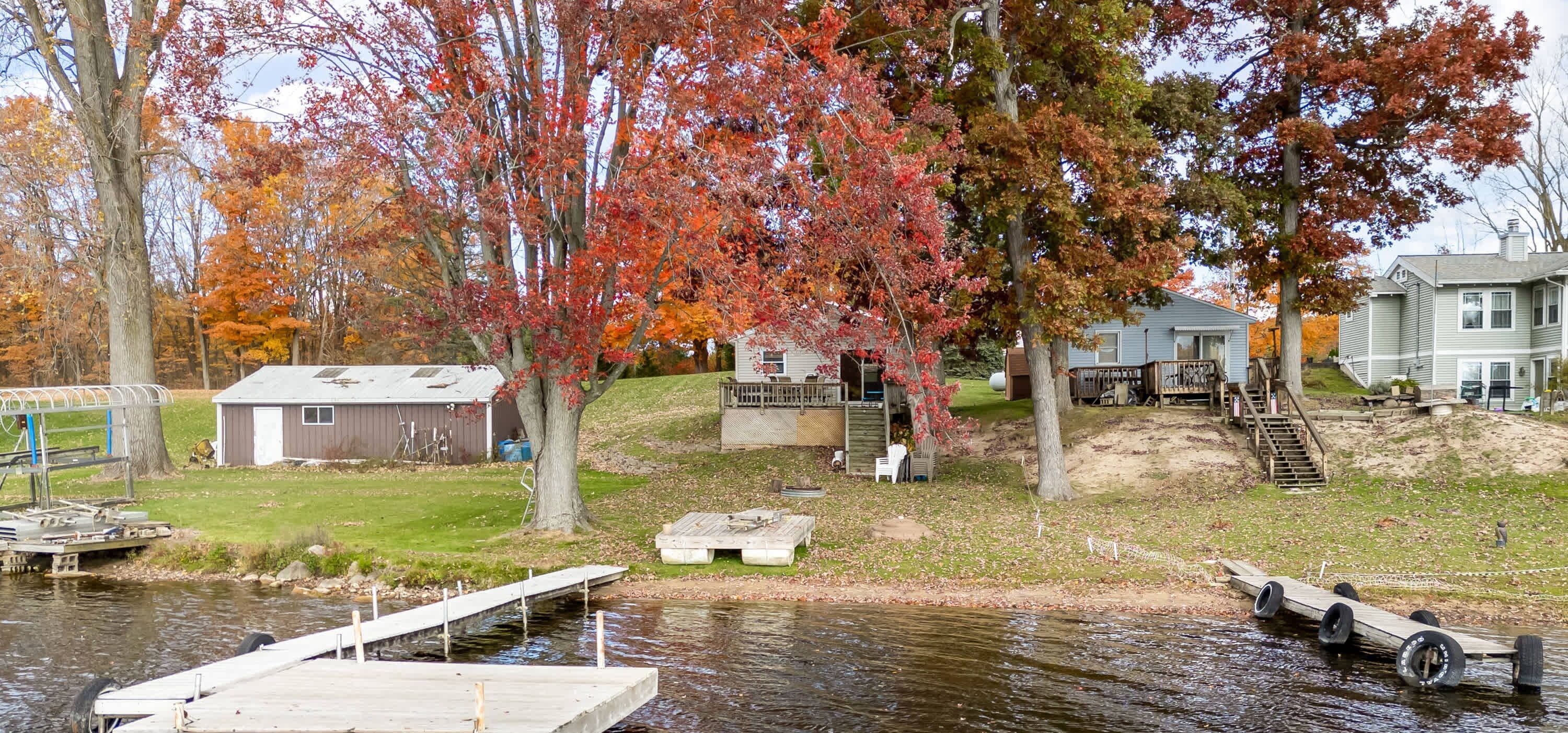 A lakeside property with a dock, a small shed, and a house with a deck.