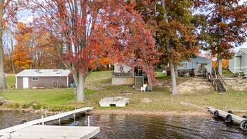 A lakeside property with a dock, a small shed, and a house with a deck.
