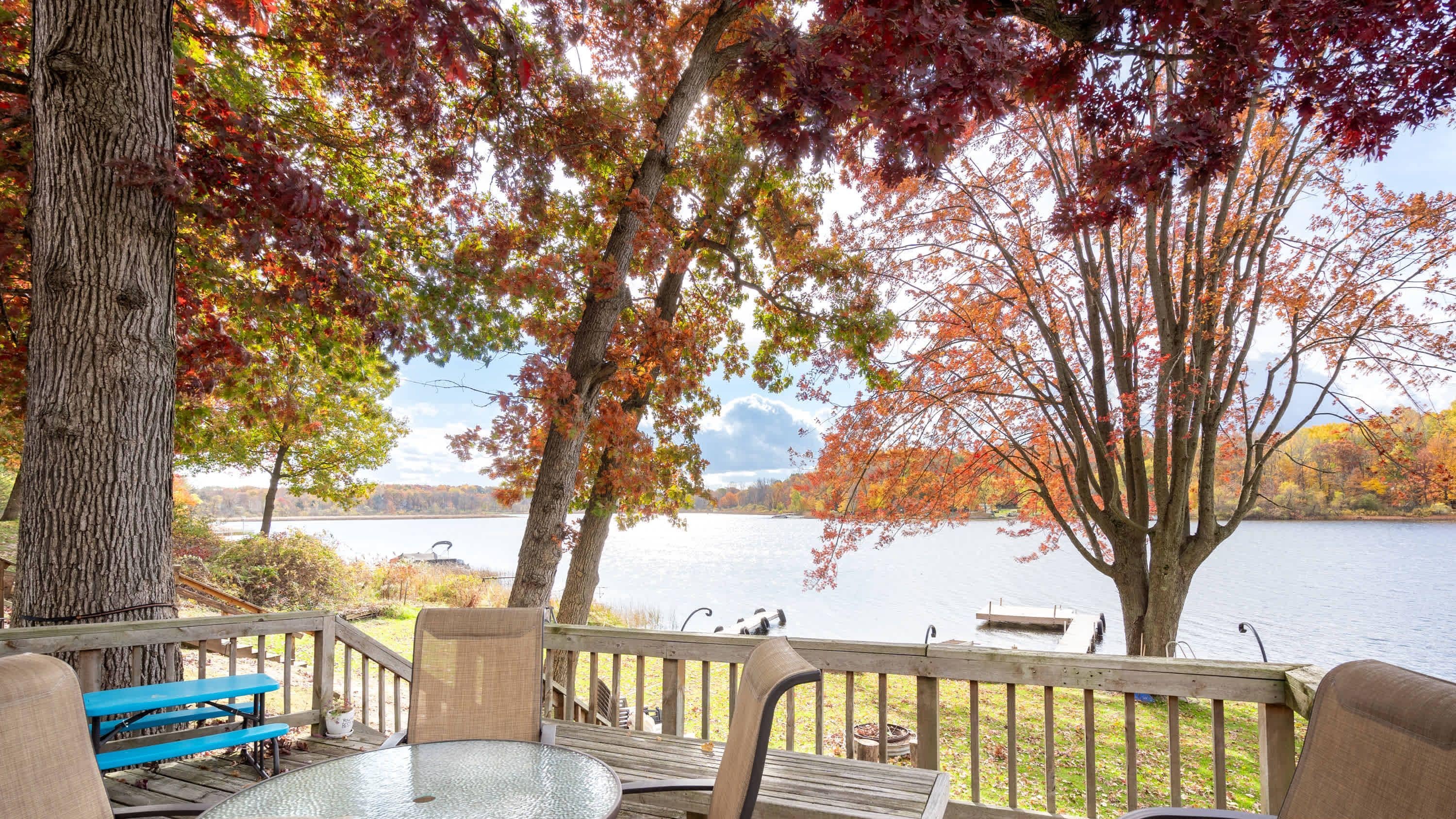 Una terraza con mobiliario exterior, con vista a un lago rodeado de follaje otoñal.