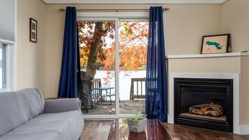 A living room with a sofa, a wooden coffee table, a fireplace, and a view of a dock and trees.