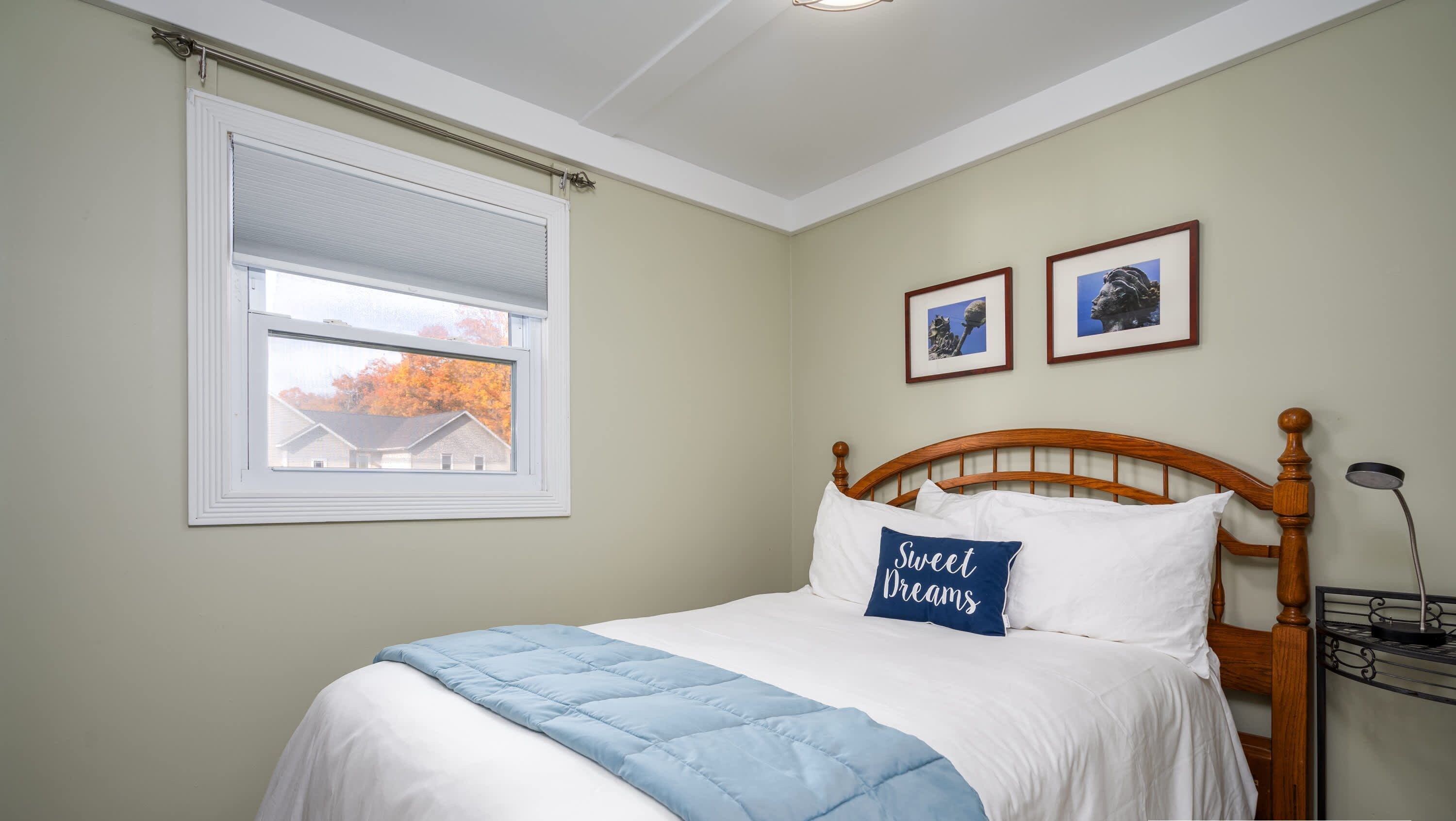 A bedroom with a bed, a window, and two framed pictures on the wall.