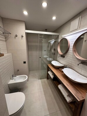 Een moderne badkamer met een douchecabine van glas, twee wasbakken en een toilet.