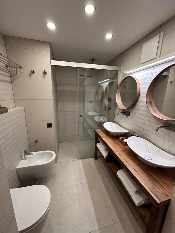 A modern bathroom with a glass-enclosed shower, two sinks, and a toilet.