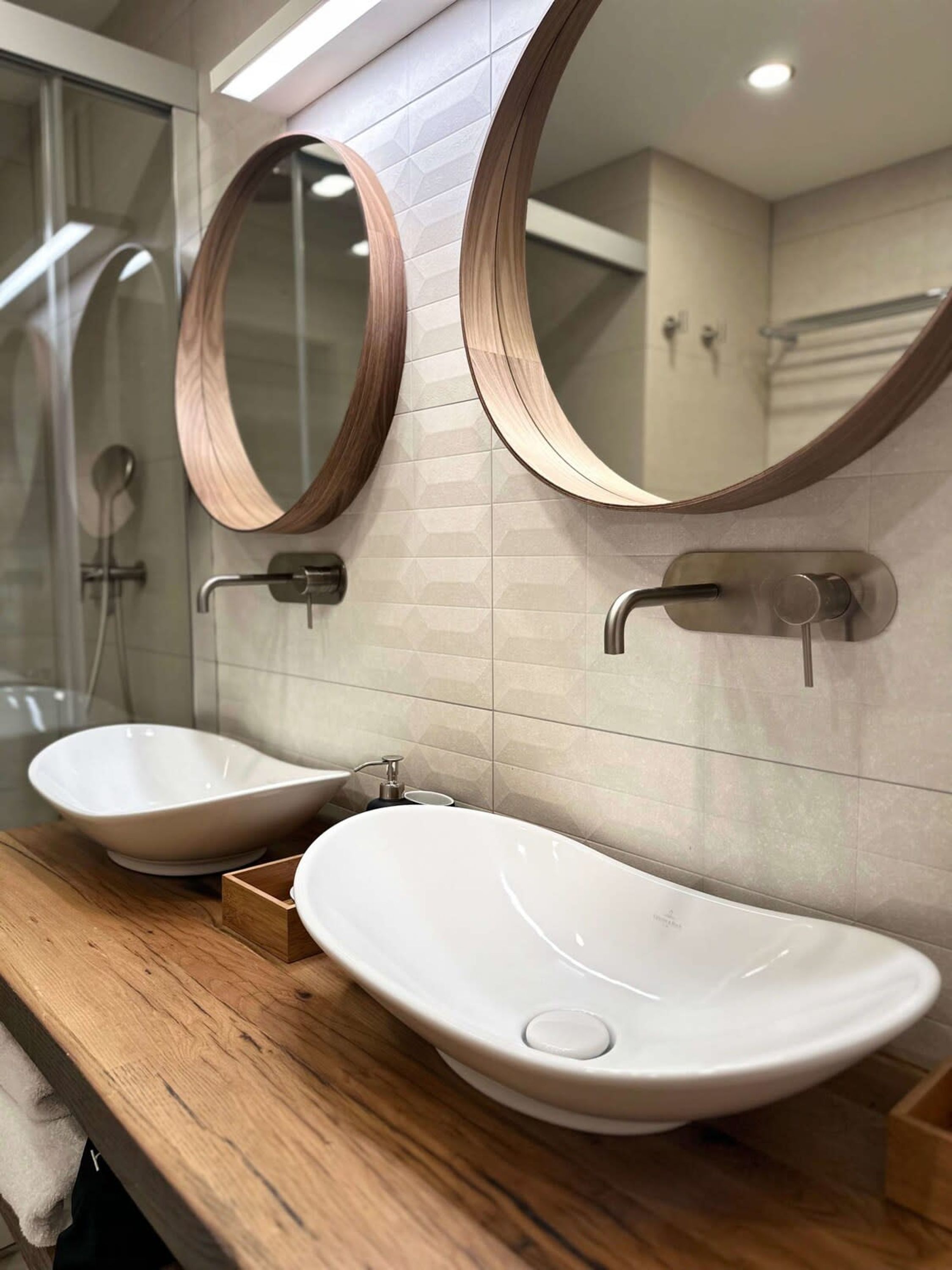 A bathroom with two white vessel sinks, wooden countertop, and two round mirrors with wooden frames.