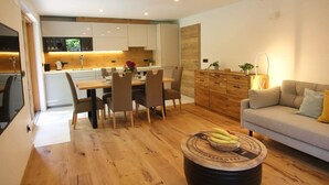 A modern kitchen with white cabinets, a dining area with a wooden table and chairs, and a living area with a sofa and a round coffee table.