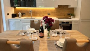 A modern kitchen with white cabinets, a wooden countertop, and a dining table set for four with glasses and a bottle of champagne.