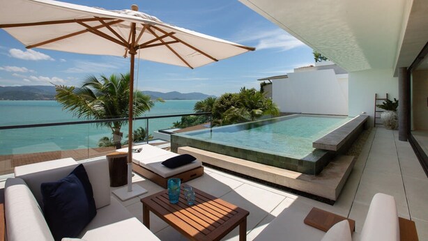 Une terrasse extérieure moderne avec une piscine, des meubles blancs et une vue sur la mer.