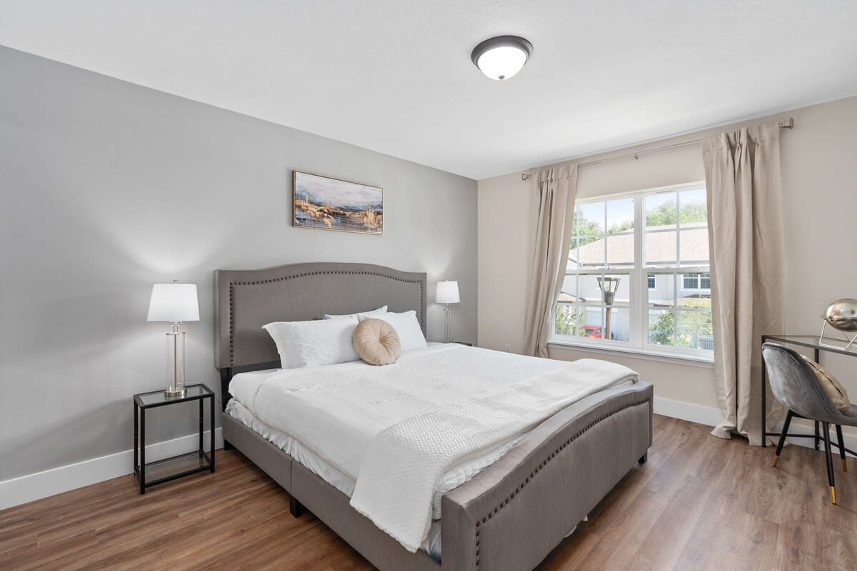 A modern bedroom with a large bed, bedside tables, a desk, and a window with curtains.