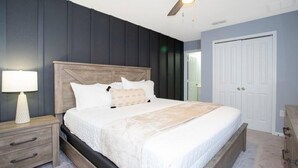 Ein Schlafzimmer mit Bett, Nachttisch, Lampe, Deckenventilator und einer Tür.