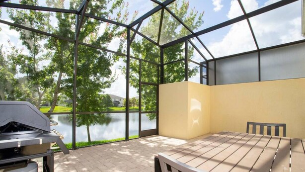 Ein überdachter Außenbereich mit Grill, Tisch und Stühlen, mit Blick auf ein Gewässer und viel Grün.