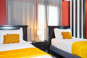 Hotellihuone, jossa on kaksi sänkyä, yöpöytä, lamppu ja ikkuna, jossa on verhot.