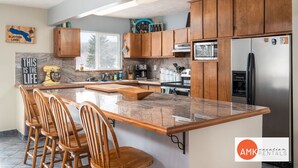A modern kitchen with wooden cabinets, granite countertops, and a built-in island with bar stools. - Life is Better by the Water at Slayton Shores (Belding)