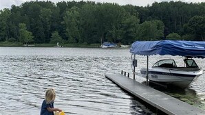 A child playing by a lake with a boat docked nearby. - Life is Better by the Water at Slayton Shores (Belding)