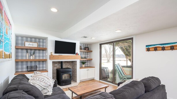 A modern living room with a sofa, a wooden coffee table, a fireplace, and a TV mounted on the wall. - Life is Better by the Water at Slayton Shores (Belding)