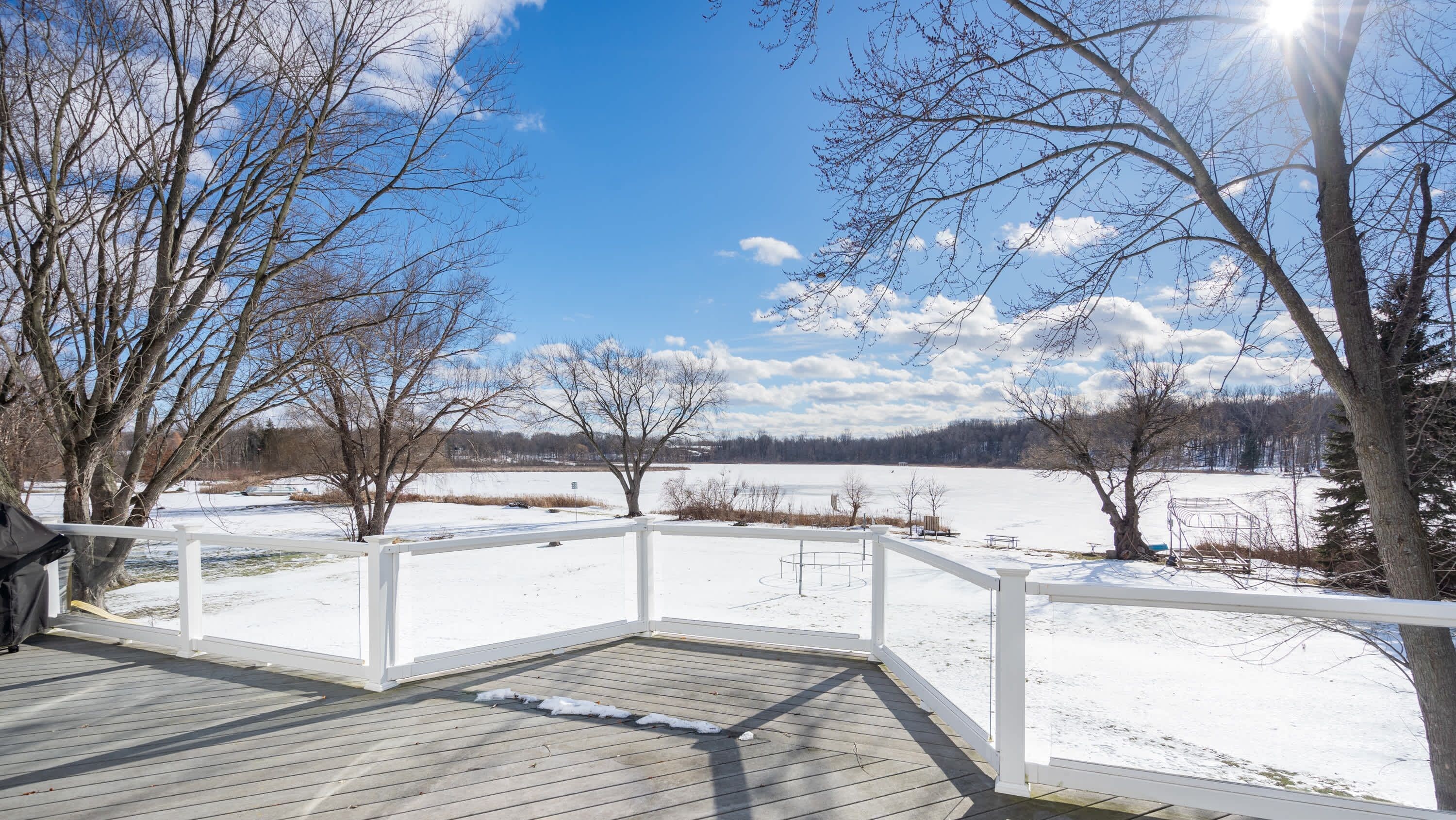 A wooden deck with a white railing overlooking a snowy landscape with trees and a clear sky.