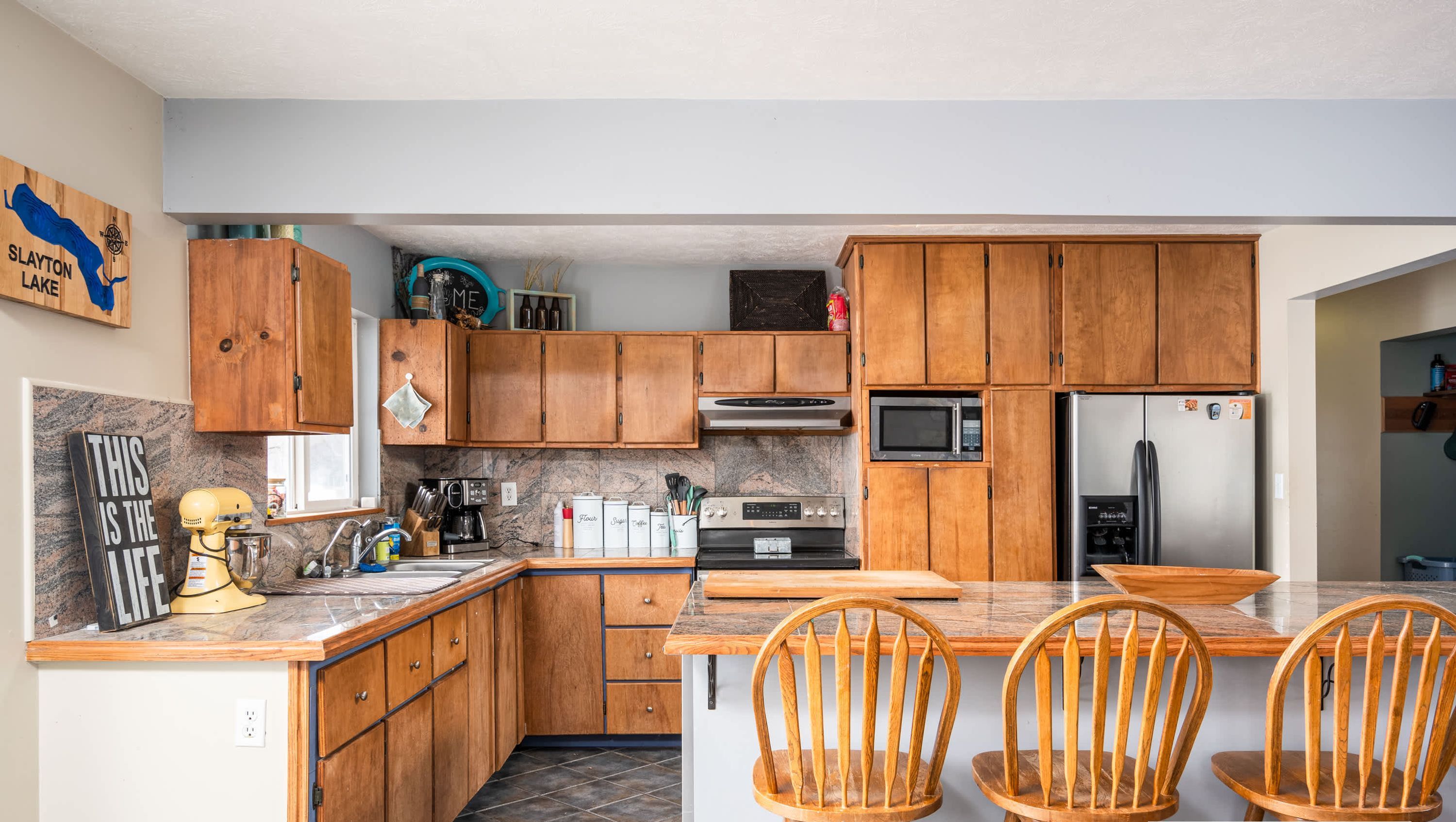 A kitchen with wooden cabinets, a microwave, a refrigerator, and a dining area with two chairs.