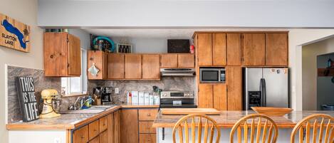 A kitchen with wooden cabinets, a microwave, a refrigerator, and a dining area with two chairs.