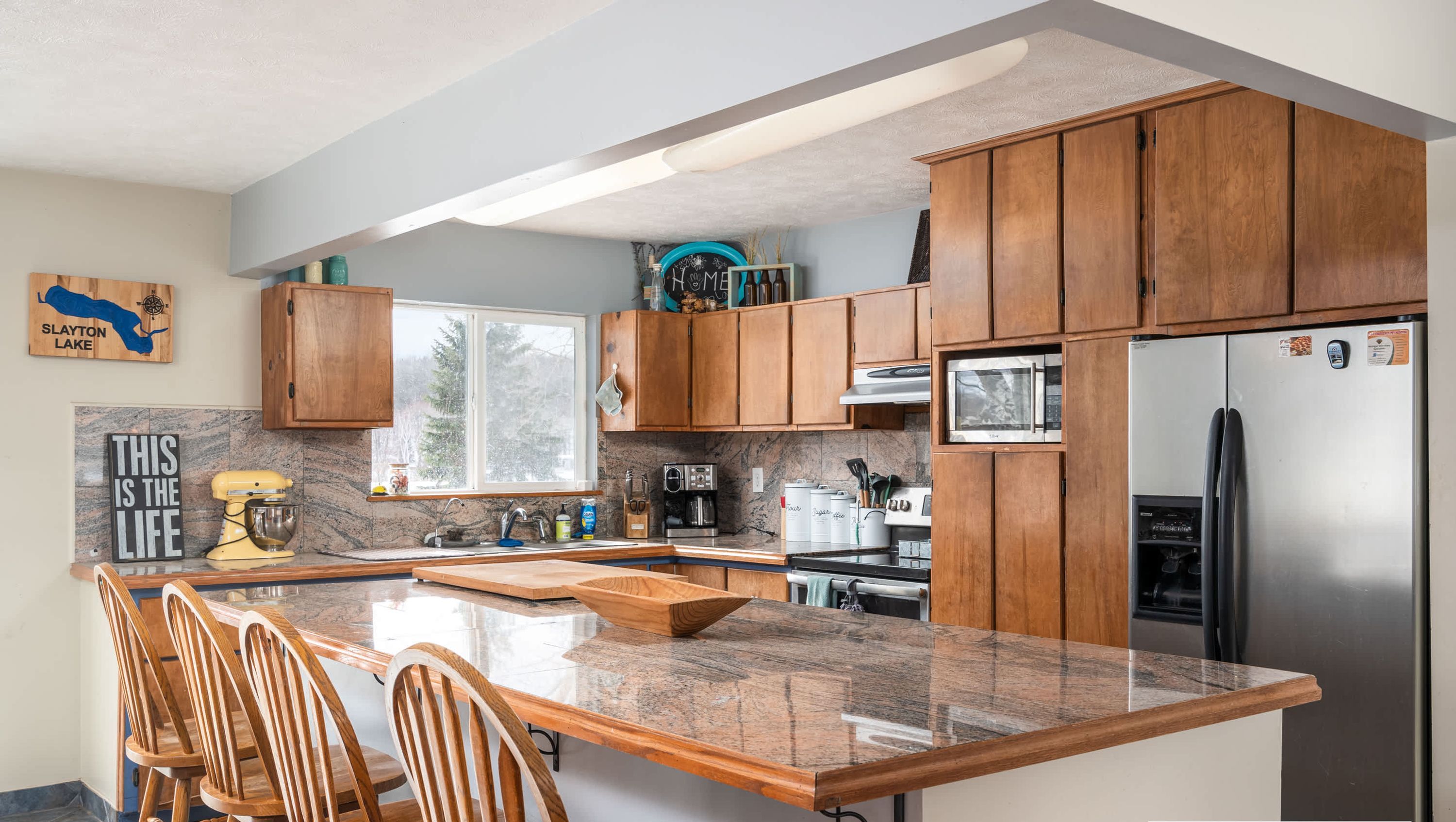 A modern kitchen with wooden cabinets, granite countertops, and a built-in island with bar stools.