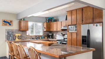 A modern kitchen with wooden cabinets, granite countertops, and a built-in island with bar stools.
