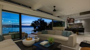 A modern living room with a large window overlooking a body of water, a sofa, coffee table, and a dining area. - Solaris 3-bedroom Beachfront Villa in Koh Samui (Koh Samui)