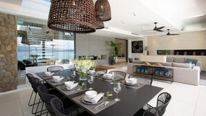 A modern dining area with a black table set for six, surrounded by black chairs. There are wicker pendant lights above the table. - Solaris 3-bedroom Beachfront Villa in Koh Samui (Koh Samui)