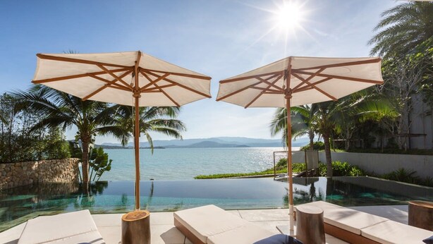 A poolside area with lounge chairs and umbrellas, overlooking a clear blue body of water and palm trees. - Solaris 3-bedroom Beachfront Villa in Koh Samui (Koh Samui)