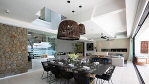 A modern dining area with a large table set for six, surrounded by black chairs, and a stone wall on one side. - Syrah 3-bedroom Beachfront Villa in Koh Samui (Koh Samui)