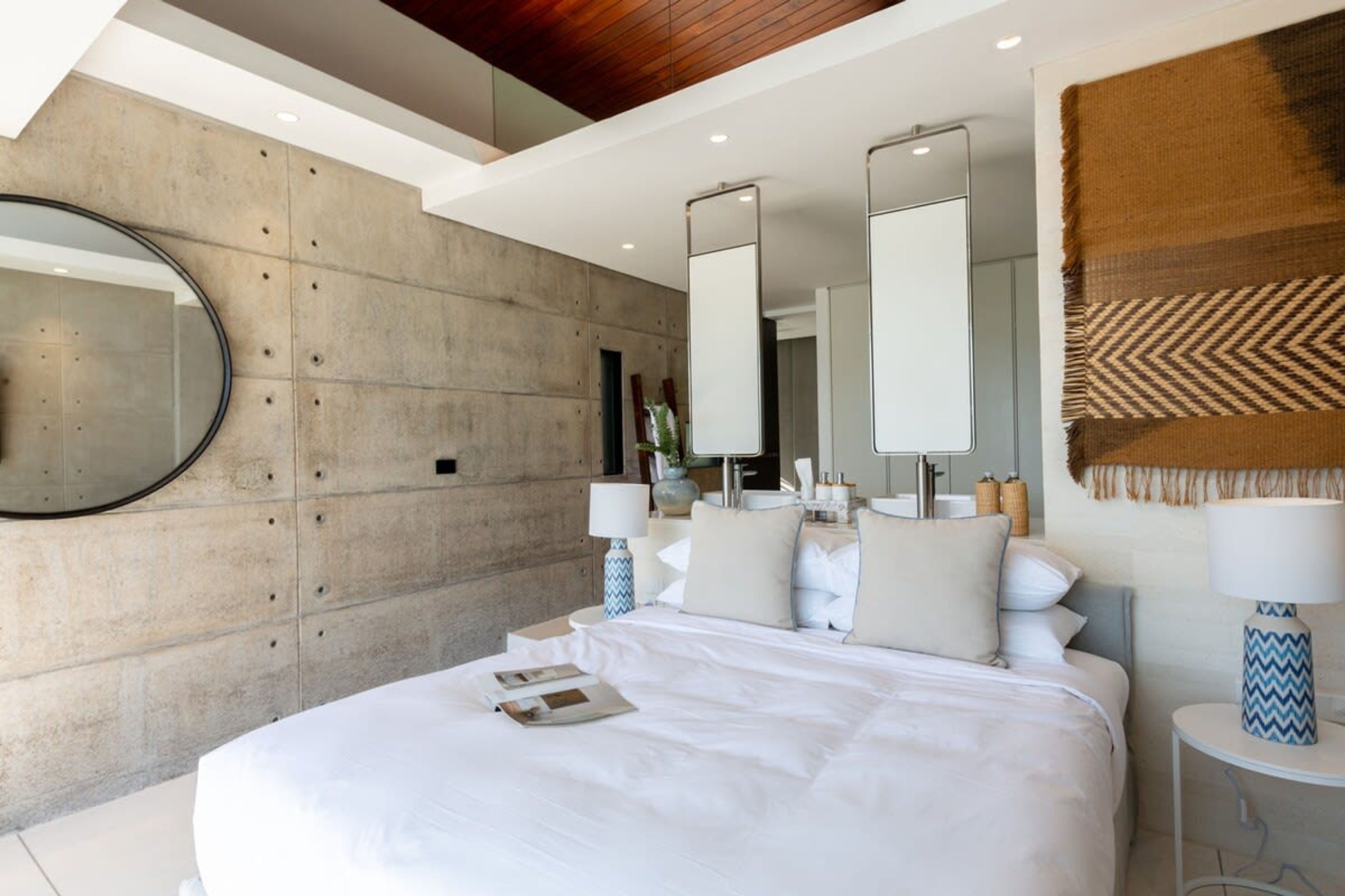 Une chambre moderne avec un grand lit, un miroir rond et une grande fenêtre.