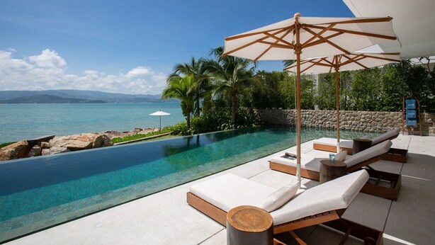 An infinity pool with lounge chairs and a large umbrella, overlooking a beach and ocean. - Syrah 3-bedroom Beachfront Villa in Koh Samui (Koh Samui)