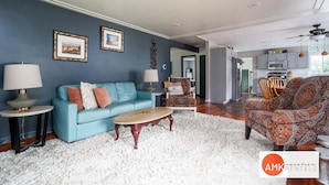 Una sala de estar con un sofá azul, un sillón estampado y una alfombra mullida blanca.