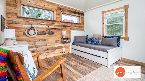 Una habitación acogedora con un muro de madera, un sofá blanco, una silla de madera y una mesita con una lámpara.