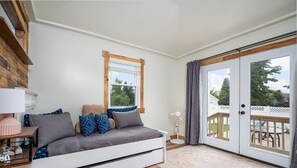 Une chambre confortable avec un lit, une table de chevet, une lampe, une fenêtre et une porte-fenêtre coulissante donnant sur une terrasse extérieure.