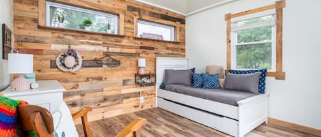 Une pièce chaleureuse avec un mur en bois, un canapé blanc, une chaise en bois et une petite table sur laquelle se trouve une lampe.