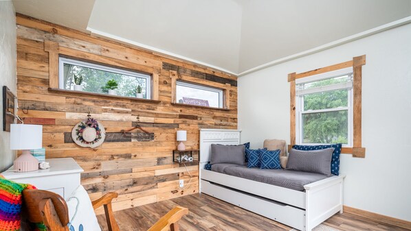 Une pièce chaleureuse avec un mur en bois, un canapé blanc, une chaise en bois et une petite table sur laquelle se trouve une lampe.
