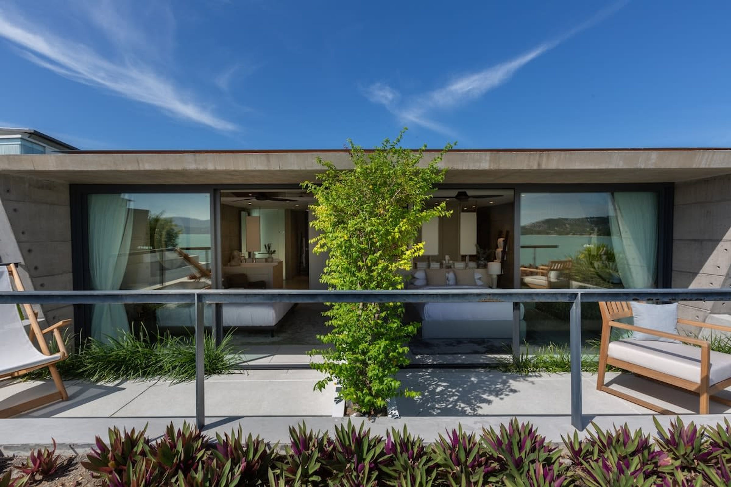 A modern house with large glass windows, a balcony with a chair, and a potted plant.